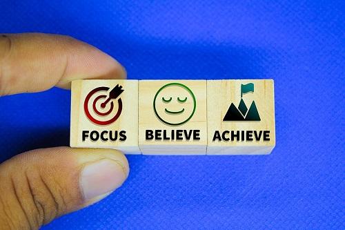 Someone holding a block with the words focus, achieve, believe